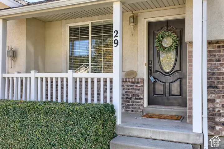 Covered front porch with white railing, stucco and brick exterior, and a dark wood-finish entry door with decorative glass