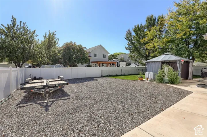 Expansive gravel area with a white privacy fence, concrete patio, and a covered gazebo