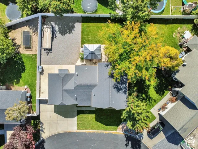 Gable roofline with dark shingles, expansive green lawn, mature trees with vibrant foliage, concrete driveway, and a gravel parking area