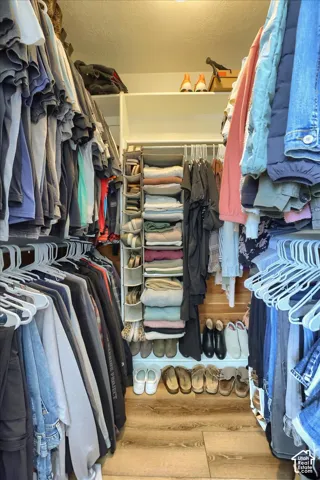 Walk-in closet featuring wood-finish flooring, white shelving, and dual clothes hanging rods
