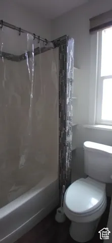 Bathtub with shower curtain, white toilet, and built-in shelving