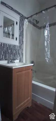Vanity with wood-finish cabinetry and white integrated sink, mosaic tile backsplash, built-in medicine cabinet, and white bathtub with chrome fixtures