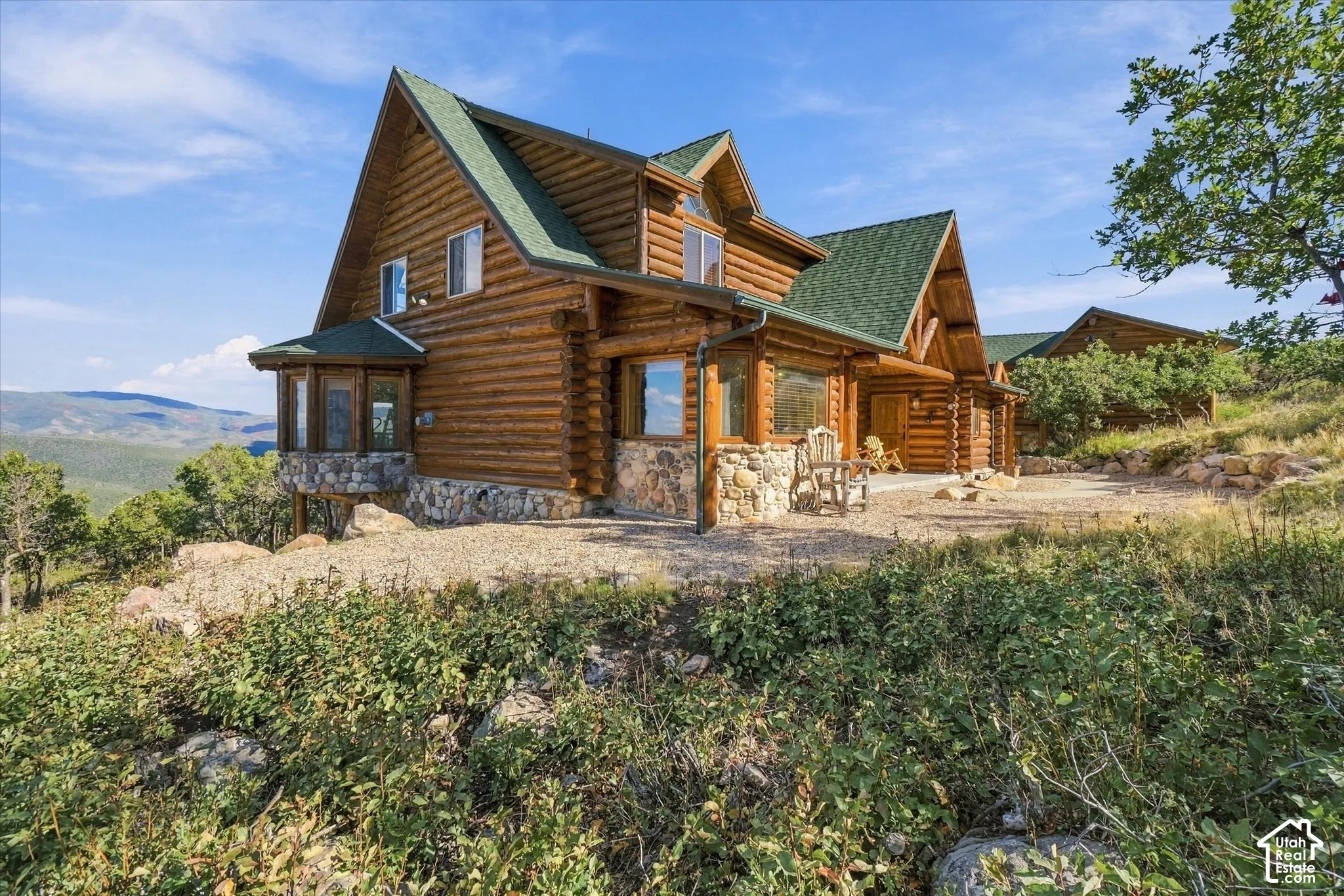 Log cabin exterior with a green shingle roof, stone foundation, and multiple gables