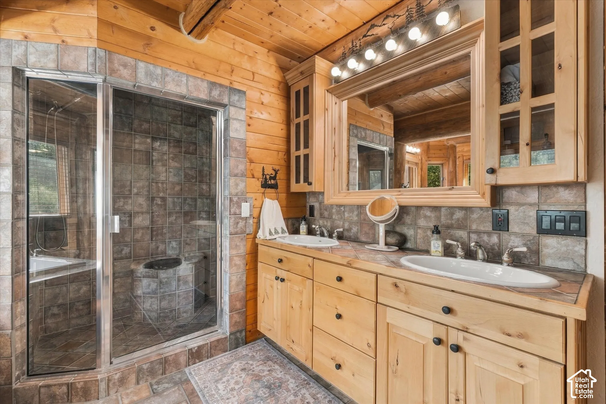 Tile-surround shower with a glass enclosure, dual vanity with undermount sinks, wood-finish cabinetry, and a full-width mirror