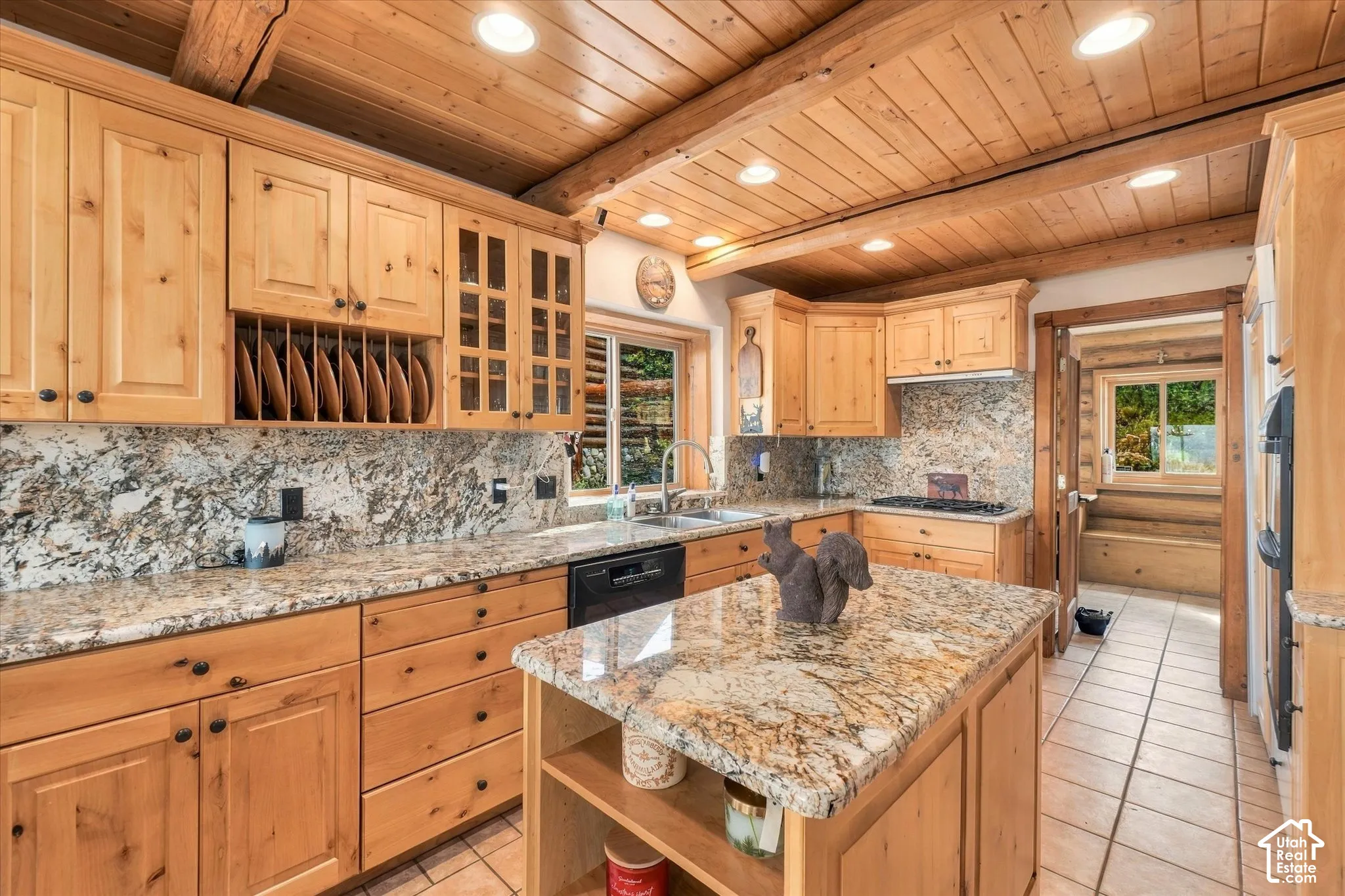 Wood-paneled ceiling with exposed beams, light wood cabinetry, granite countertops, tile flooring, and integrated appliances