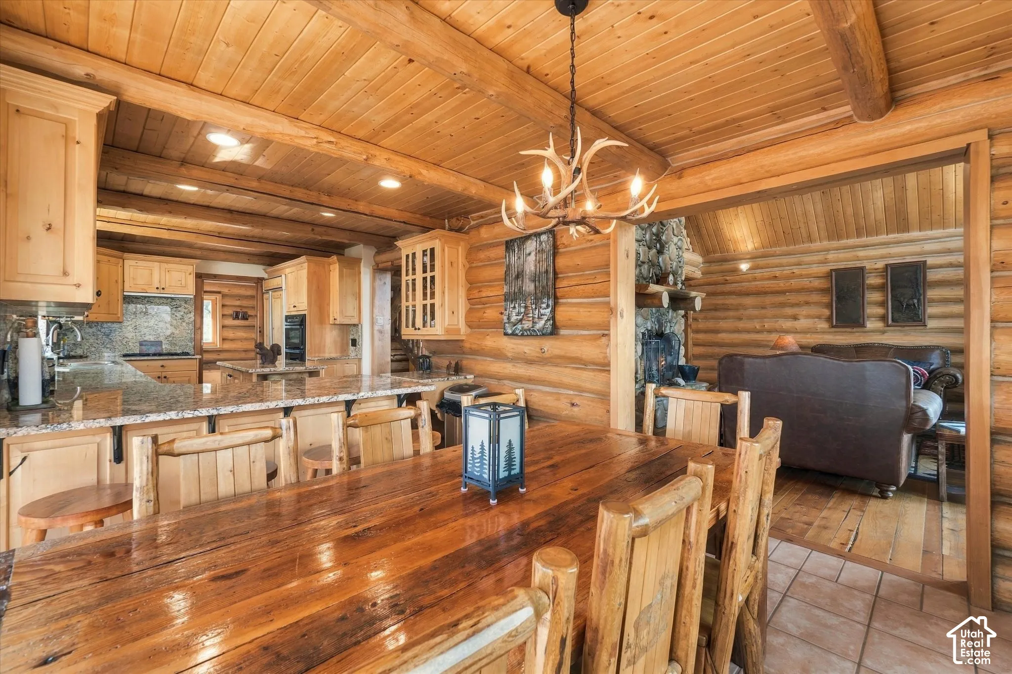 Log and wood-panel interior finishes, kitchen with light wood cabinetry and stone countertops, built-in cooktop, and a natural stone fireplace