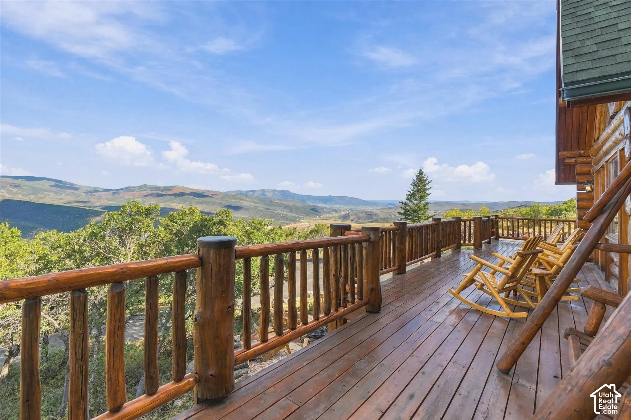 Expansive outdoor deck with natural wood railing, log-style exterior, and distant mountain scenery