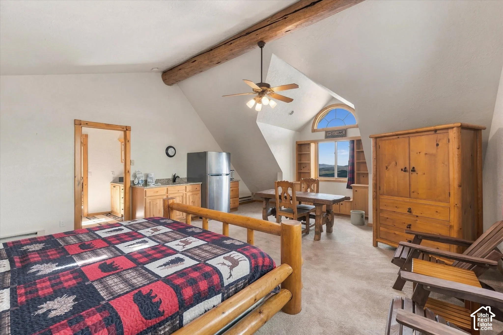 Vaulted ceiling with exposed wood beam, ceiling fan, arched window, wood-finish cabinetry, and built-in shelving