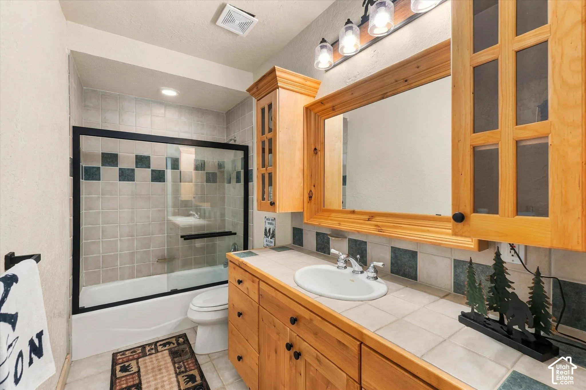 Bathroom featuring a wood-finish vanity with an integrated sink, tile countertop, and wood-framed mirror