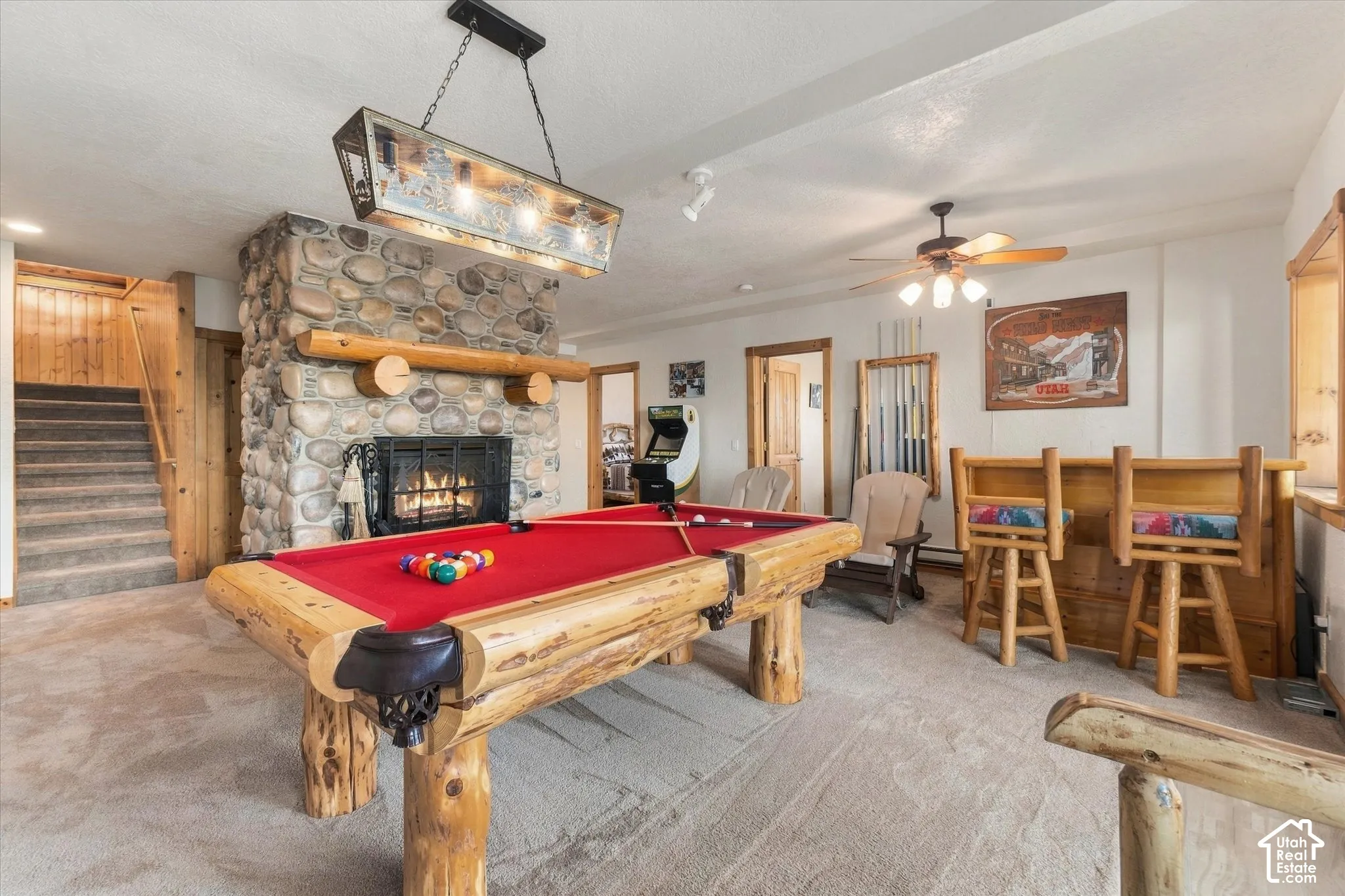 Stone-faced fireplace with a wood mantle, wood-paneled staircase, and built-in wood bar