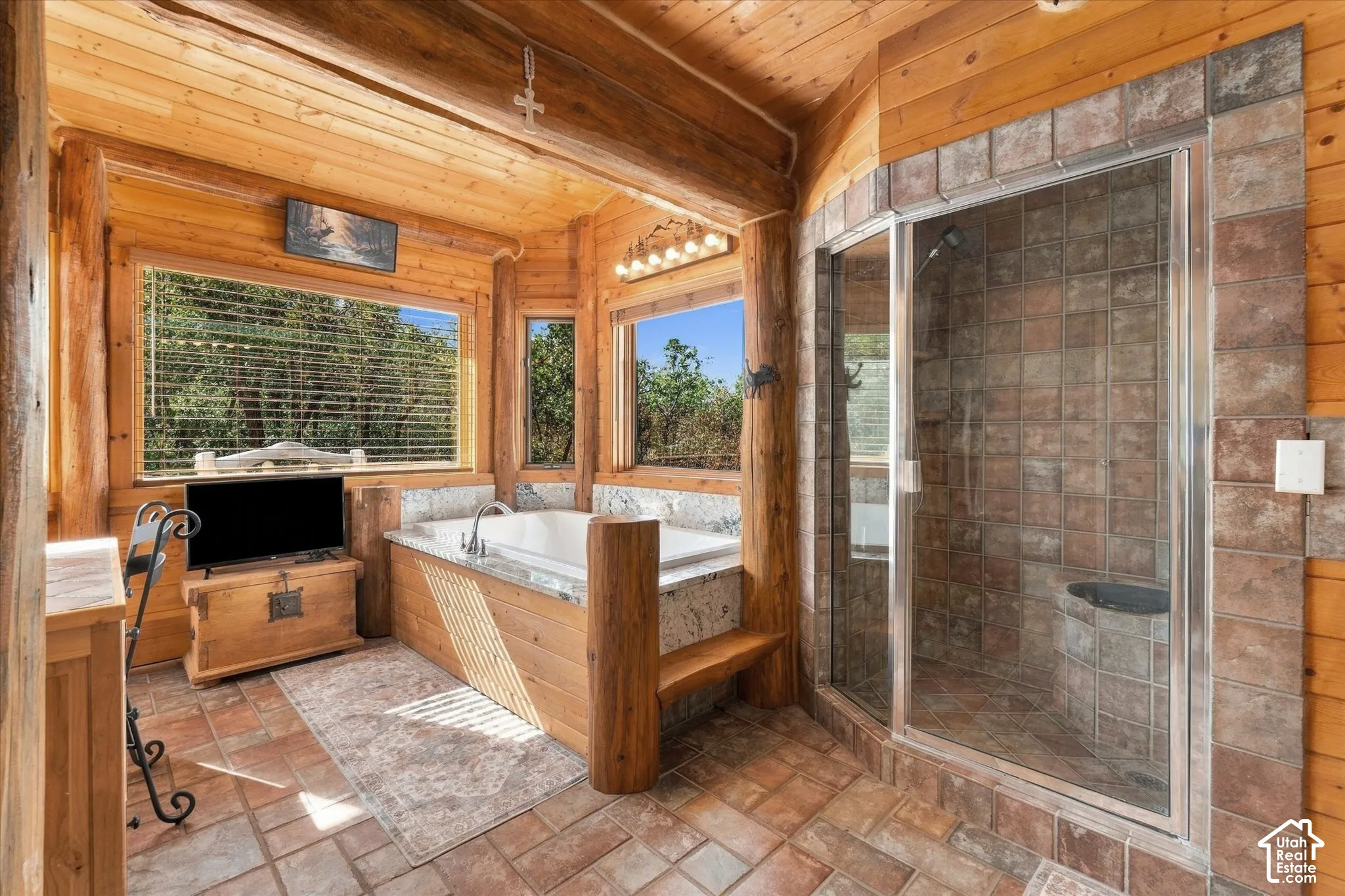 Spacious bathroom featuring wood-clad walls and ceiling, a built-in soaking tub with a light-toned countertop, a glass-enclosed shower with tiled walls and a built-in bench, and multiple windows
