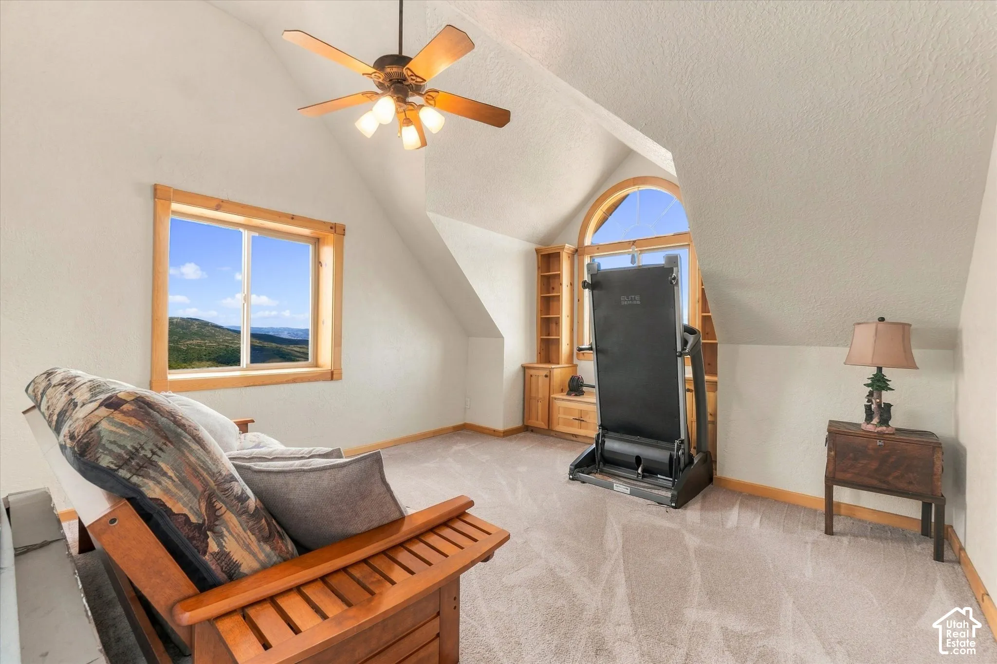 Pitched ceiling room featuring a ceiling fan, a window with wood trim, built-in shelving, an arched window, and carpet flooring