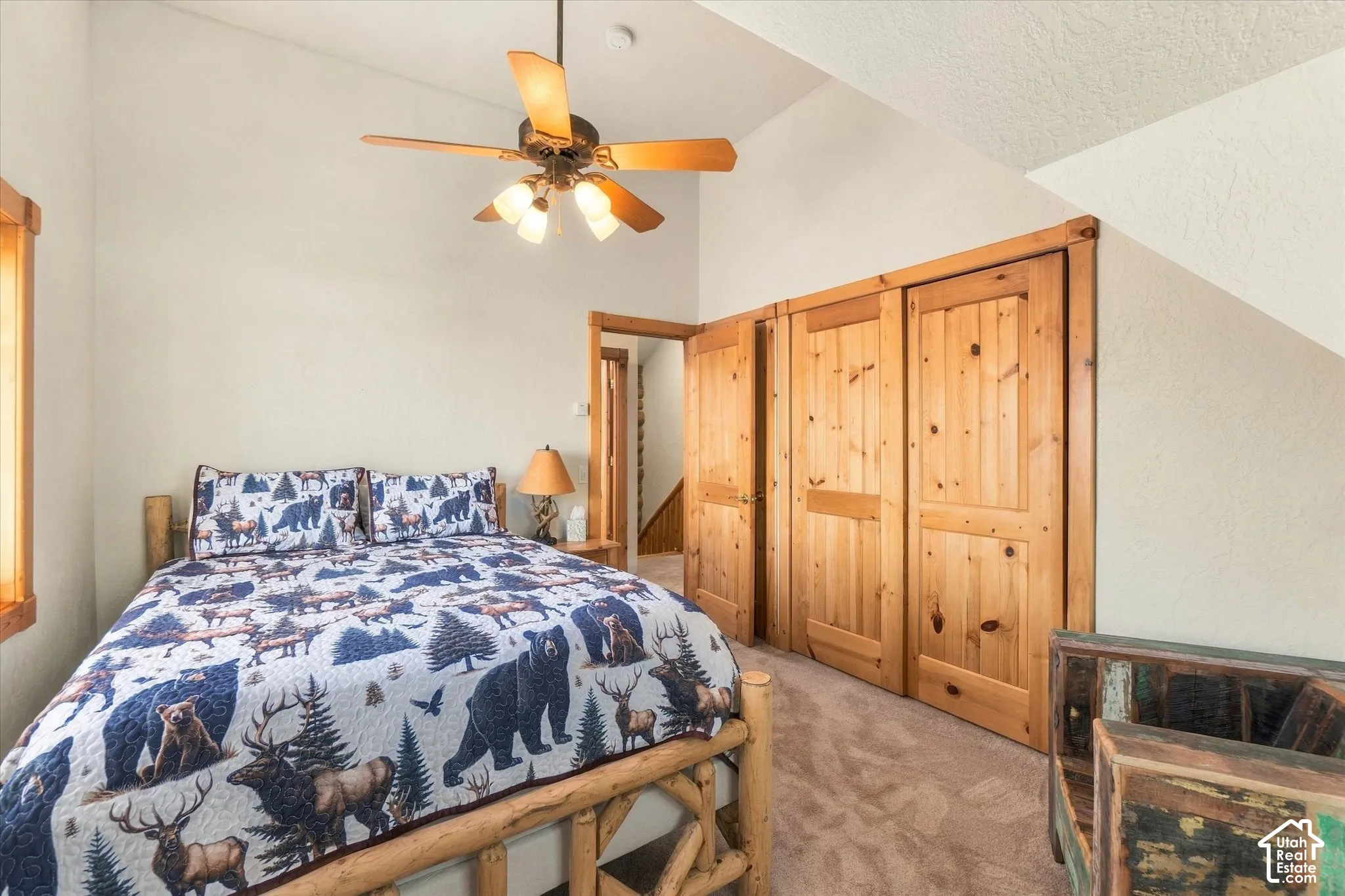 Carpeted room with a vaulted ceiling, wood-finish ceiling fan with integrated lighting, and natural wood bi-fold closet doors