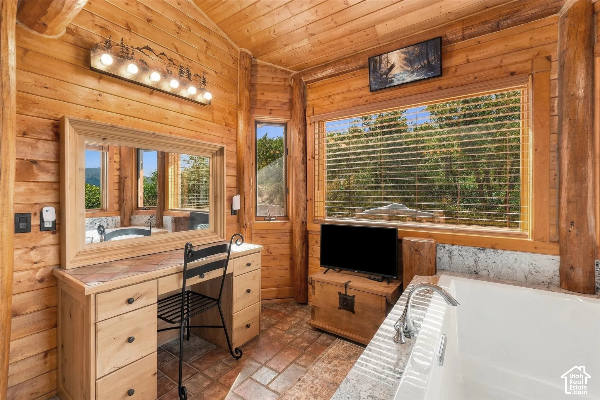 Wood paneling throughout, built-in vanity with tiled countertop, large soaking tub, and multiple windows providing natural light