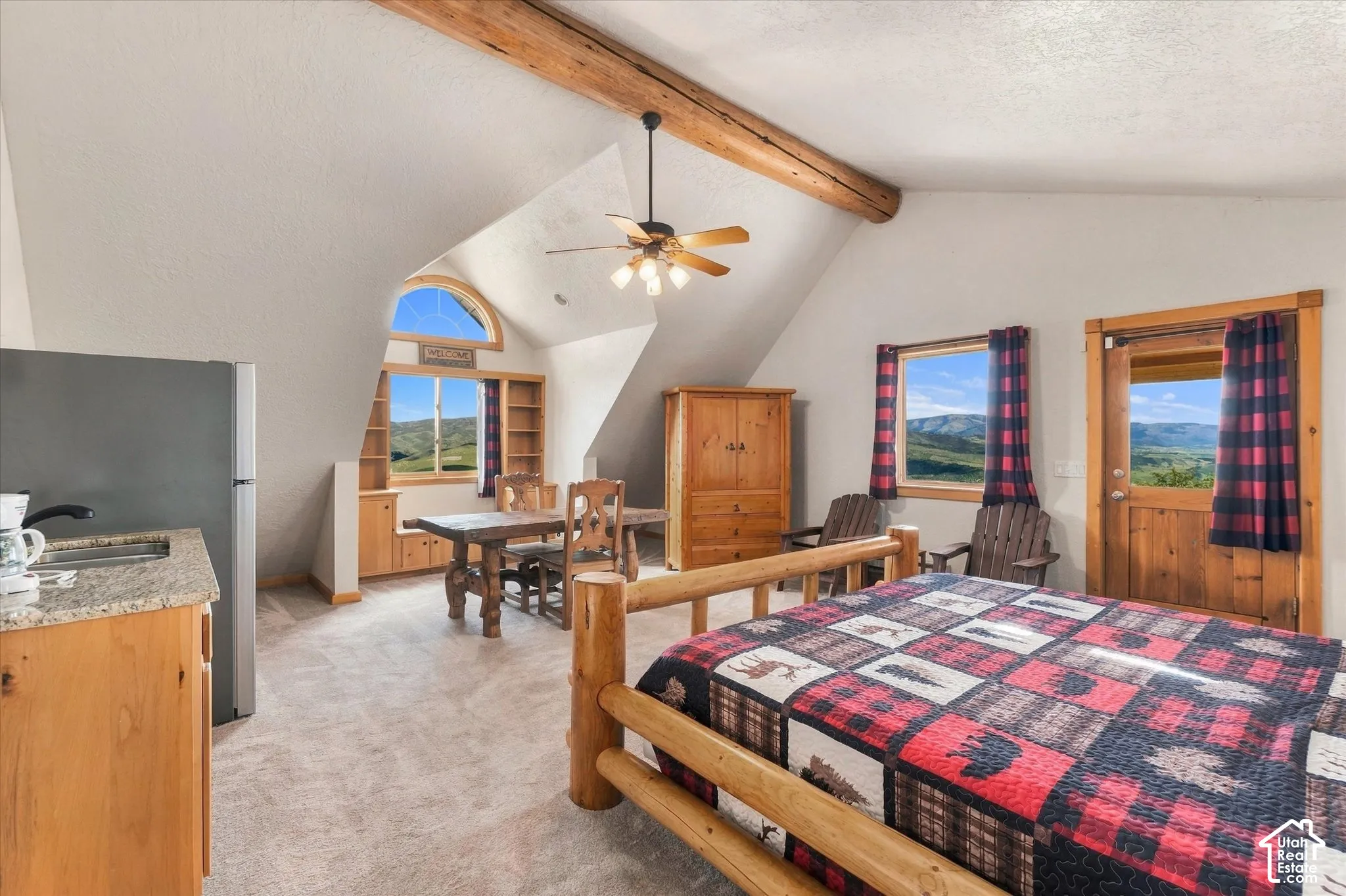 Carpeted room with exposed wooden beams, a ceiling fan, and sloped ceilings