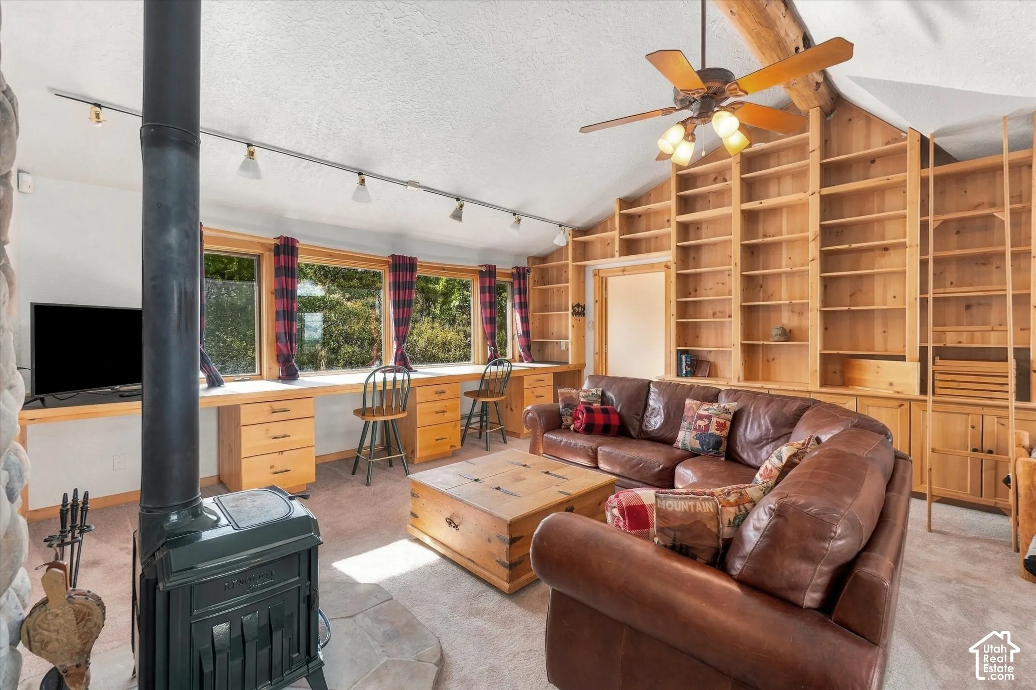 Built-in wood shelving, wood-finish ceiling fan, wood-finish window desks with storage, wood-finish built-in cabinetry, and a black wood-burning stove
