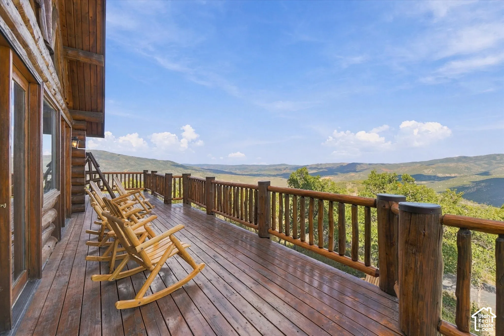 Expansive outdoor deck featuring wood-plank flooring, a rustic wood railing, and a mountainous backdrop