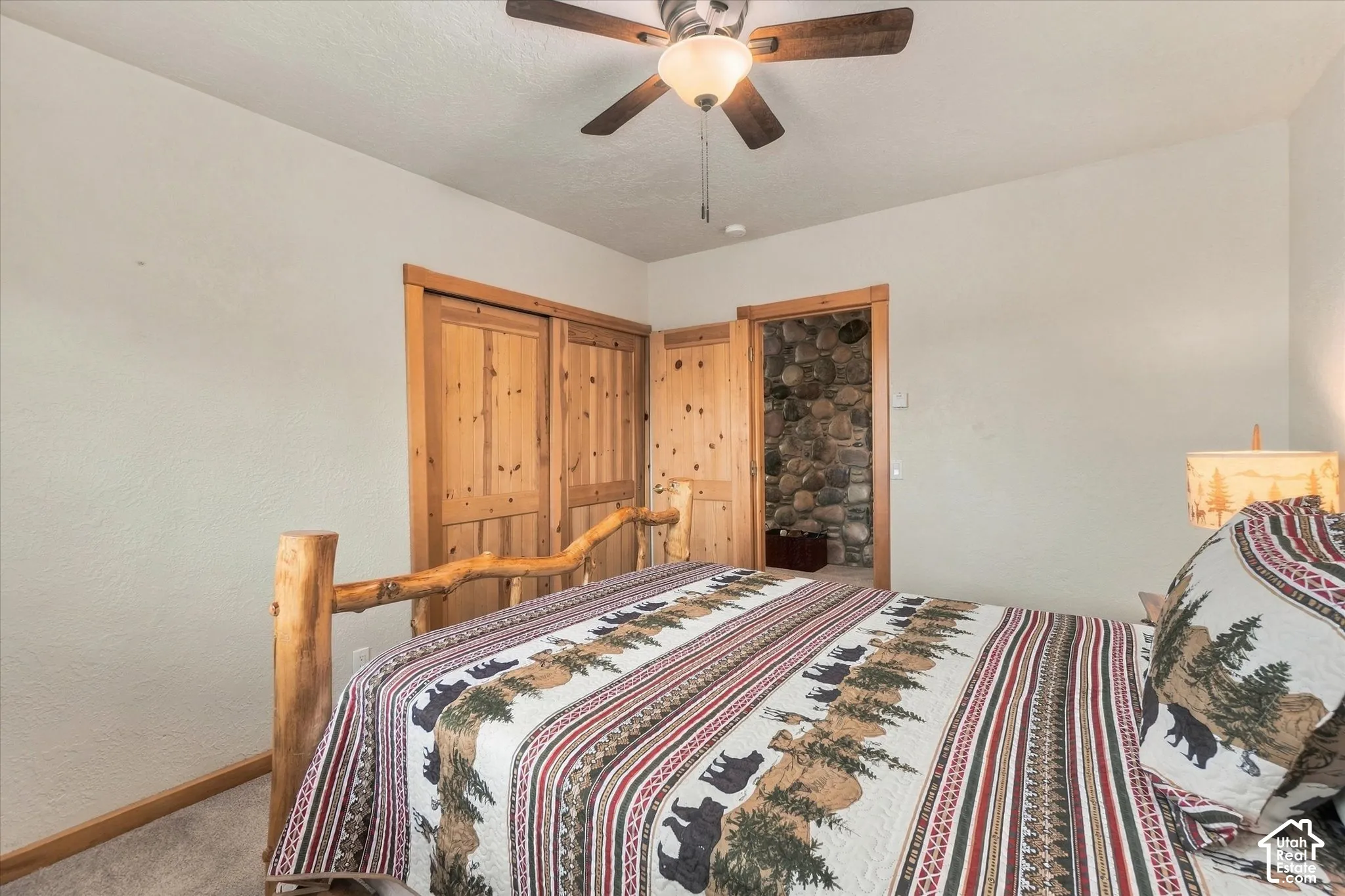 Ceiling fan with integrated lighting, wood-finish bi-fold doors, wood-finish trim, wood-finish bed frame, and a stone-clad wall feature