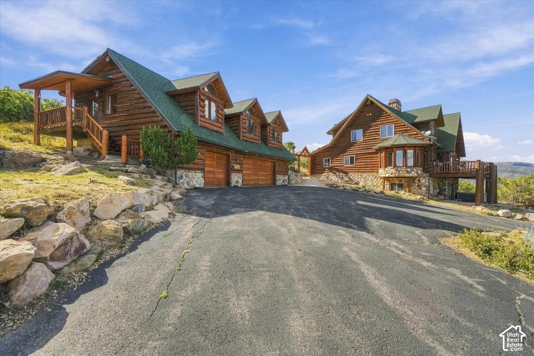 Log-sided exterior with a green roof, stone accents, multiple garages, and an expansive deck