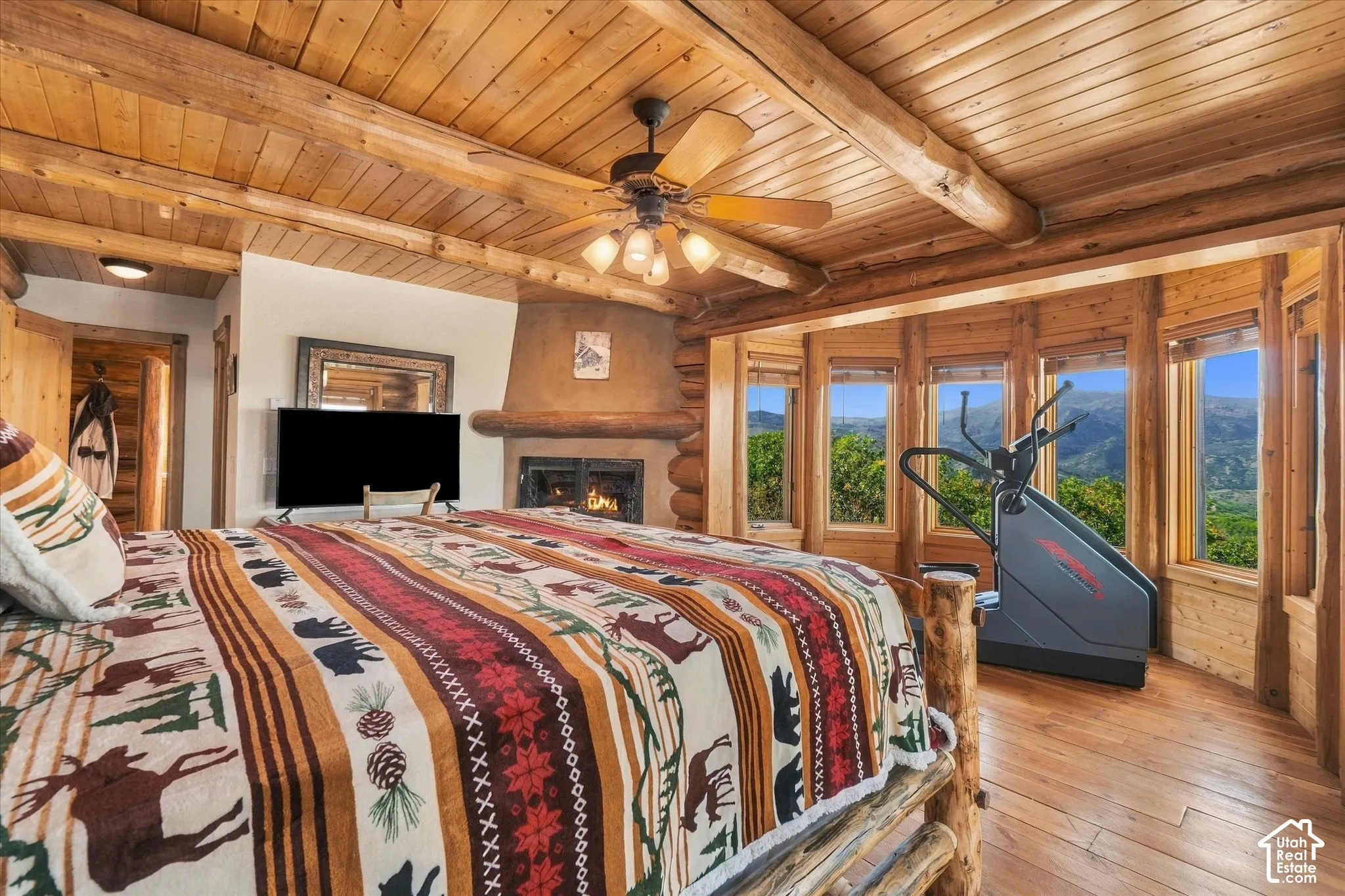 Wood-paneled ceilings with exposed log beams, built-in fireplace with a stucco surround, bay window with multiple individual panes, and wood-finish flooring