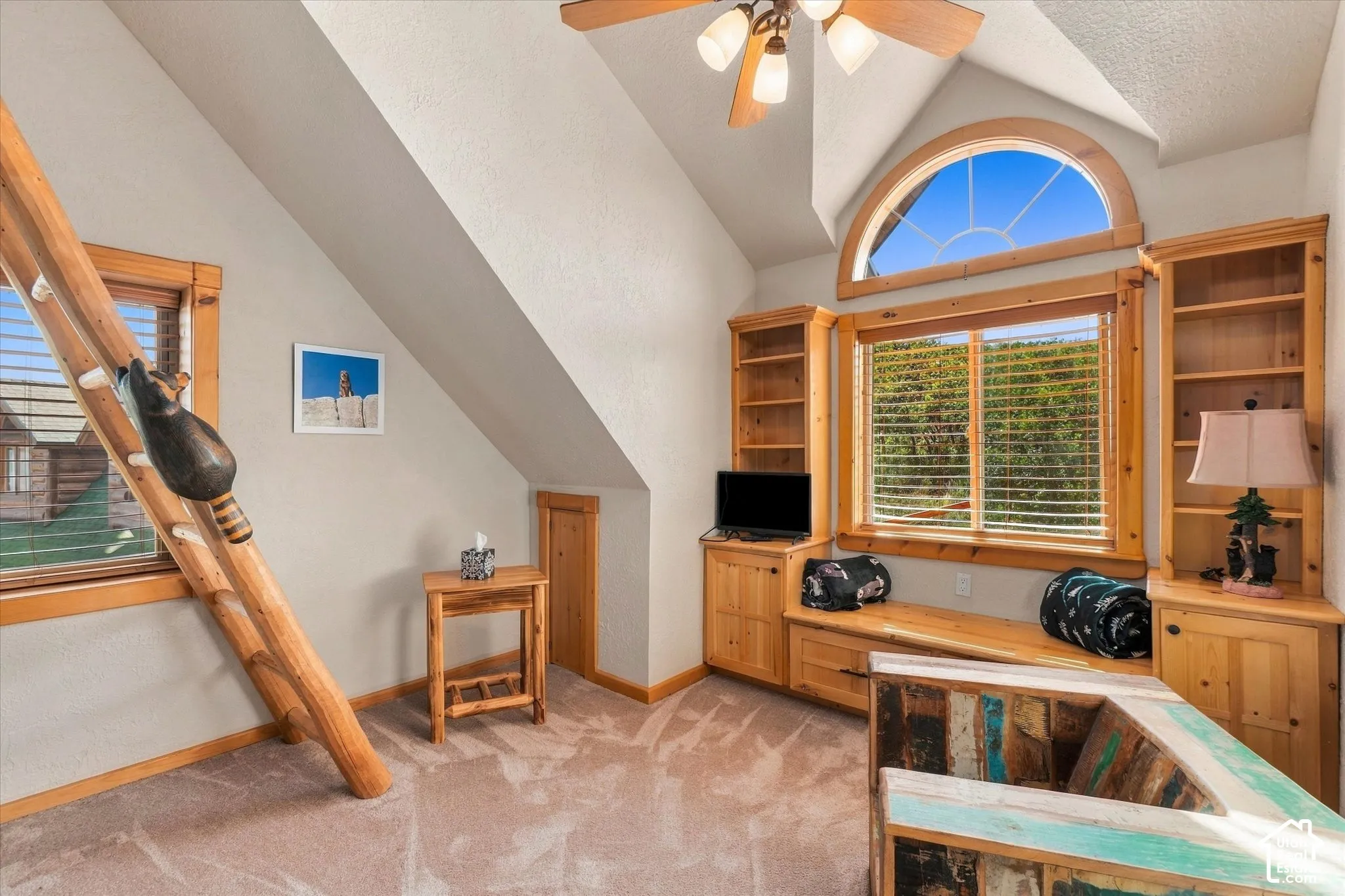 Vaulted ceiling with a ceiling fan, built-in shelving, an arched window, and wood-frame windows