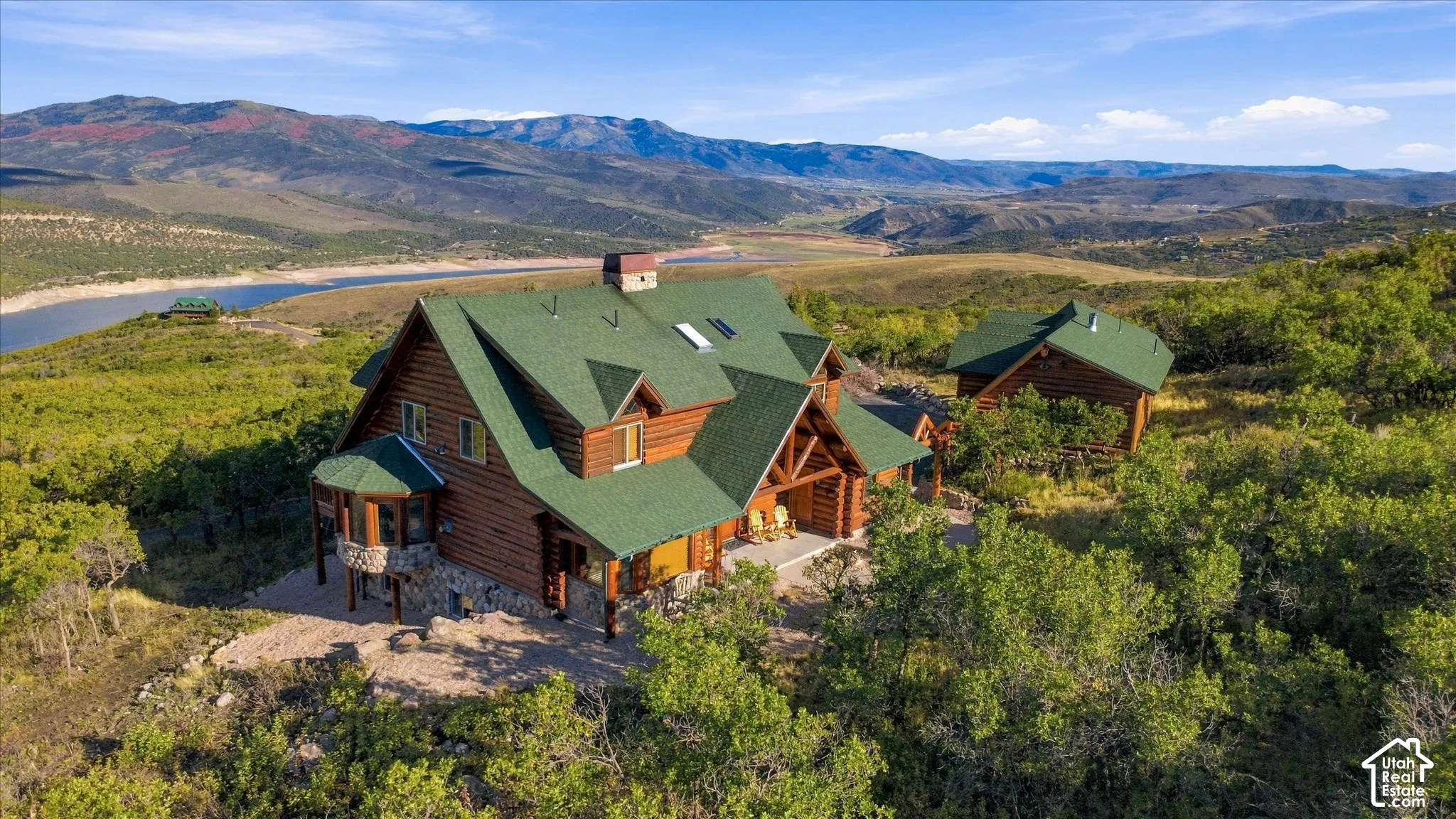 Log home construction with a green roof, multiple dormer windows, stone foundation accents, and a covered porch