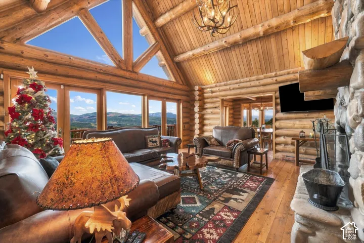 Expansive great room featuring a stone fireplace, wood-finish flooring, exposed log walls, and a vaulted ceiling with triangular window elements