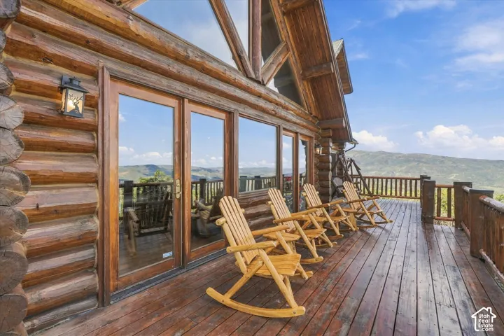 Expansive wood deck with a full wood railing, featuring a log cabin exterior, large glass doors, and a decorative outdoor wall light