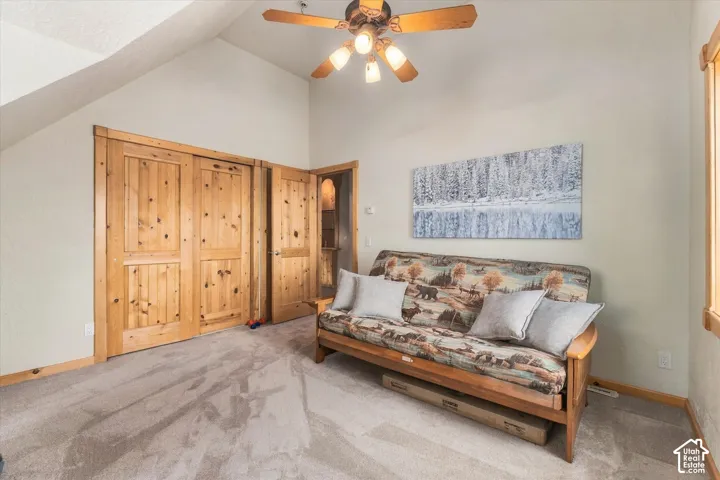 Vaulted ceiling with a ceiling fan, carpet flooring, natural wood doors, and natural wood window trim