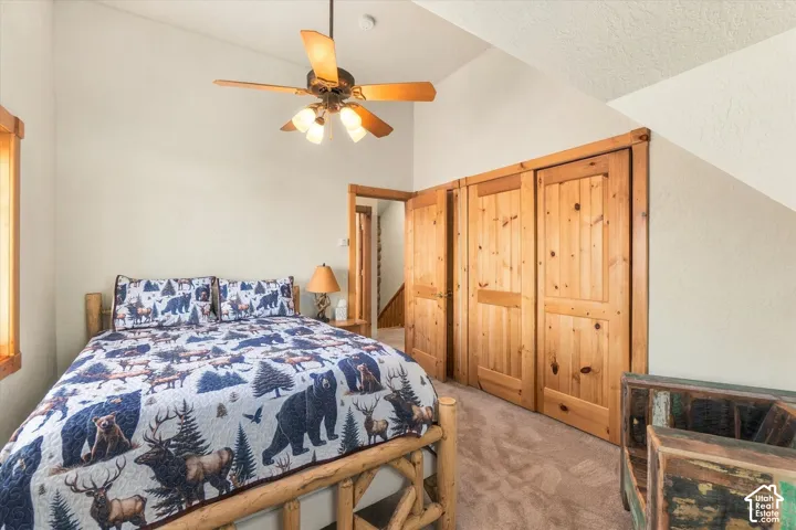 Carpeted room with a vaulted ceiling, wood-finish ceiling fan with integrated lighting, and natural wood bi-fold closet doors