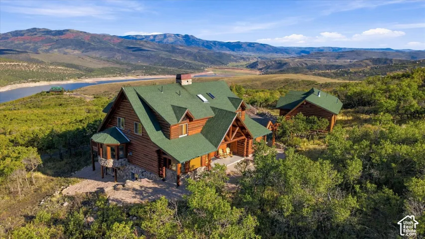 Log home construction with a green roof, multiple dormer windows, stone foundation accents, and a covered porch