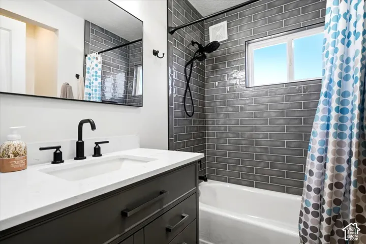 Bathroom featuring a white bathtub, gray subway tile surround, white window, dark gray vanity with a white countertop, and a rectangular mirror