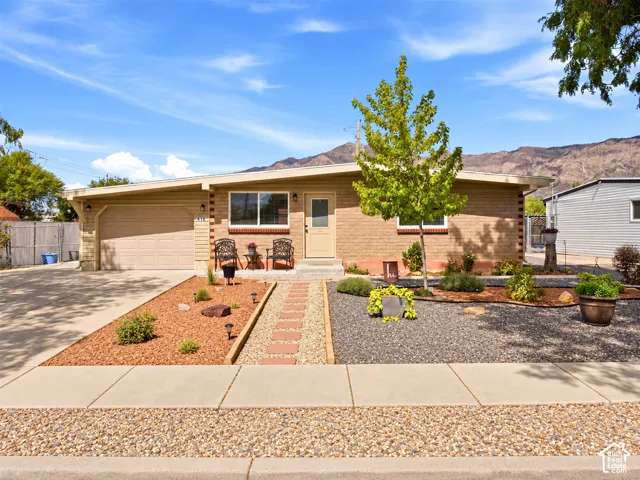 Brick exterior with an attached garage, landscaped rock gardens, and a paved driveway