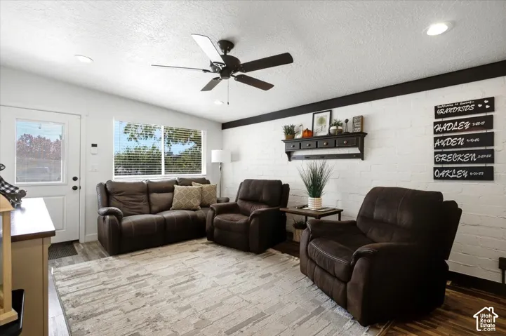 Wood-finish flooring, recessed lighting, ceiling fan, and white brick accent wall