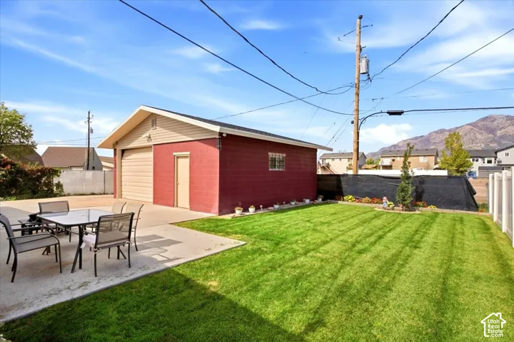 Detached garage with two roll-up doors, concrete patio, and a manicured lawn