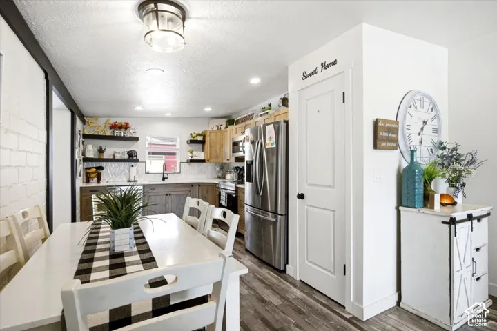Kitchen and dining area featuring wood-finish flooring, white brick-patterned wall, recessed lighting, and stainless steel appliances
