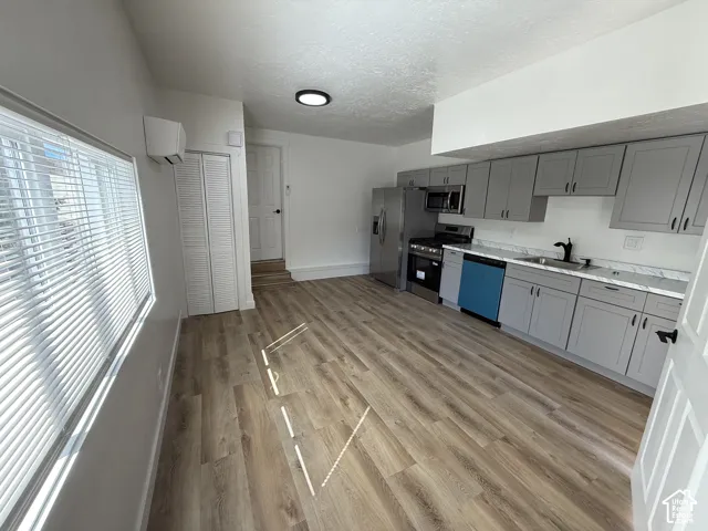 Open-concept living space with wood-finish flooring, a full kitchen featuring gray cabinetry and stainless steel appliances, and a window with blinds