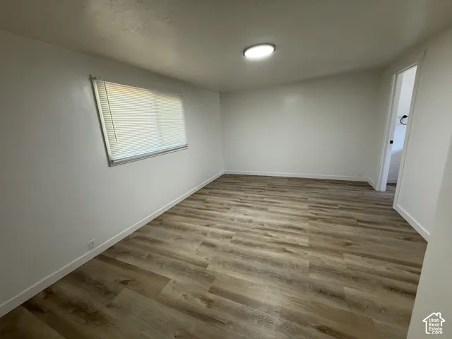 Spacious room featuring wood-finish flooring, white walls, and a ceiling-mounted light fixture