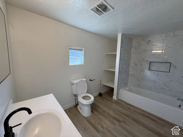 White vanity with an integrated sink and a matte black faucet, wood-finish flooring, built-in shelving, white subway tile tub surround, and a rectangular shower niche