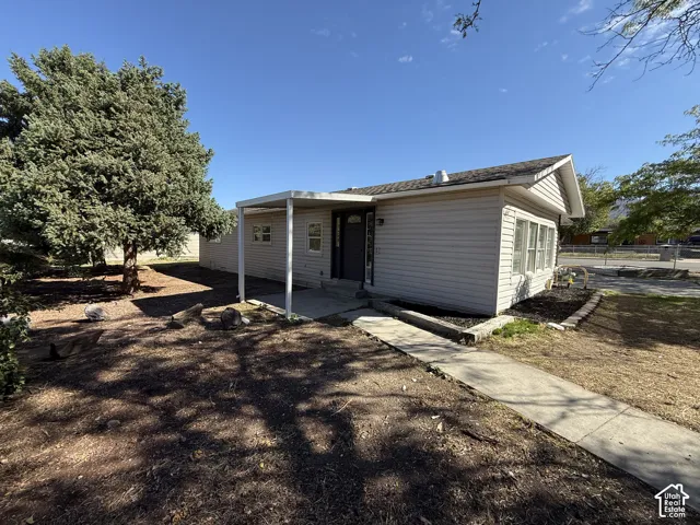 Siding exterior with a covered patio, concrete walkway, and established trees