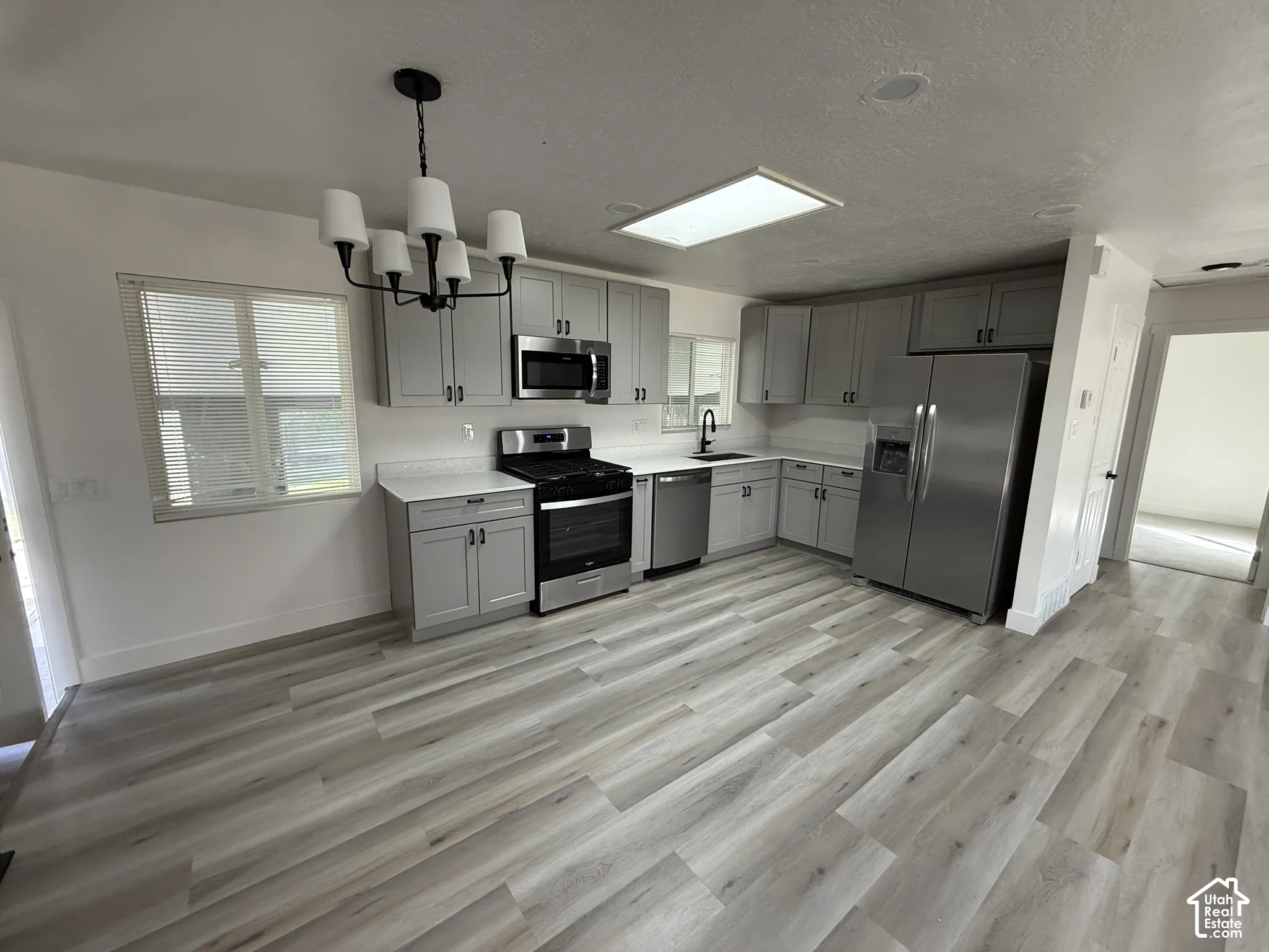 Kitchen featuring light wood-finish flooring, gray cabinetry with black hardware, white countertops, and stainless steel appliances