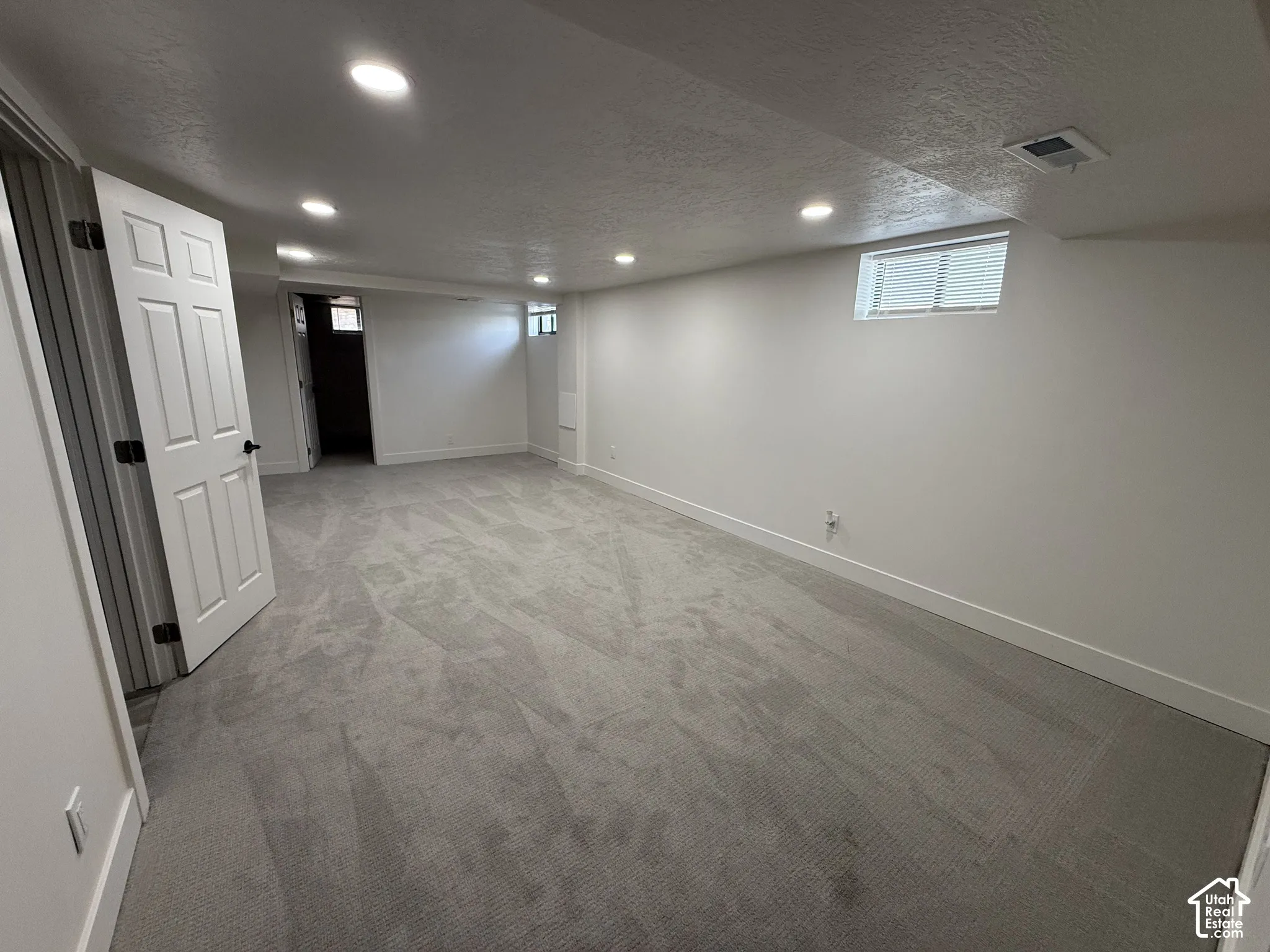 Spacious room with gray carpeting, recessed ceiling lighting, white walls, and a white paneled door