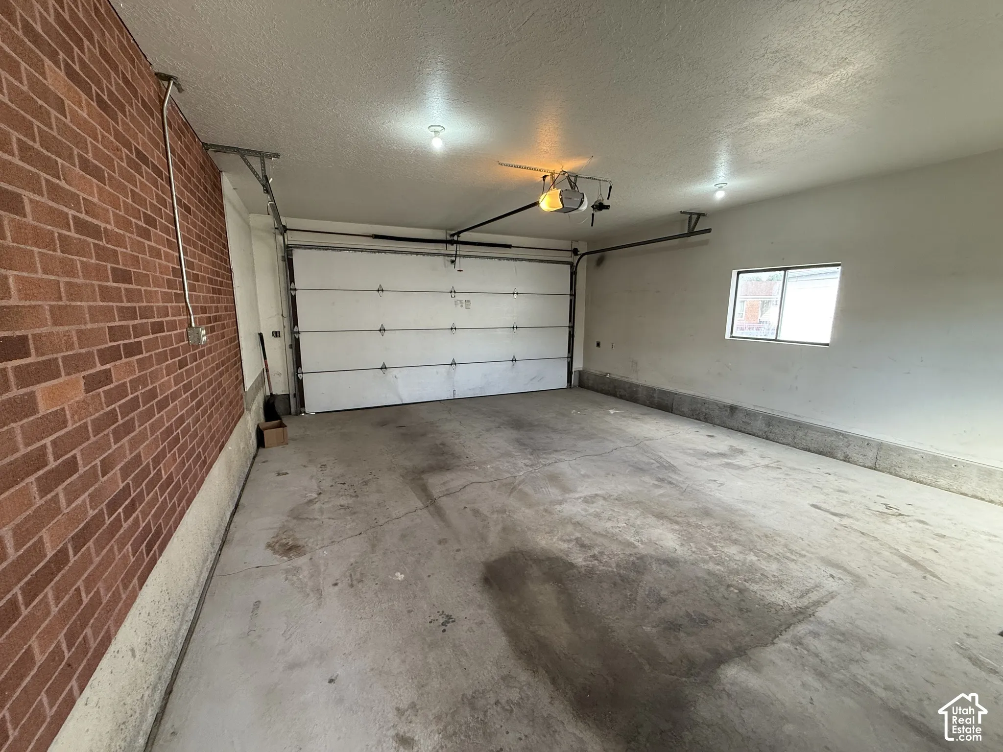 Brick wall interior, concrete flooring, overhead garage door, single-pane window, and overhead lighting