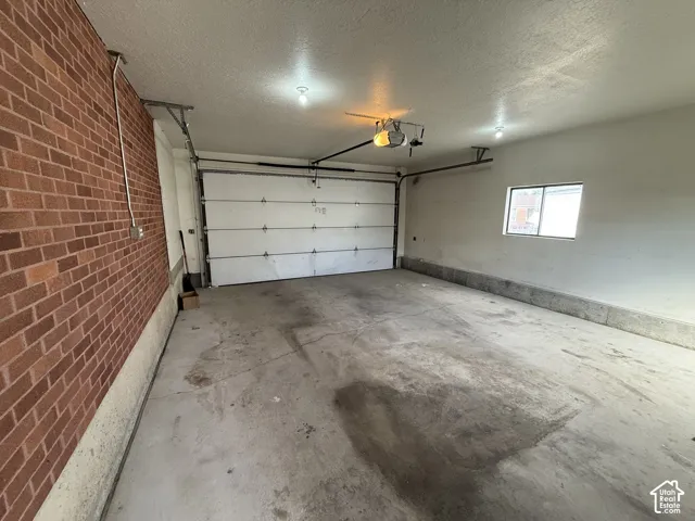 Brick wall interior, concrete flooring, overhead garage door, single-pane window, and overhead lighting