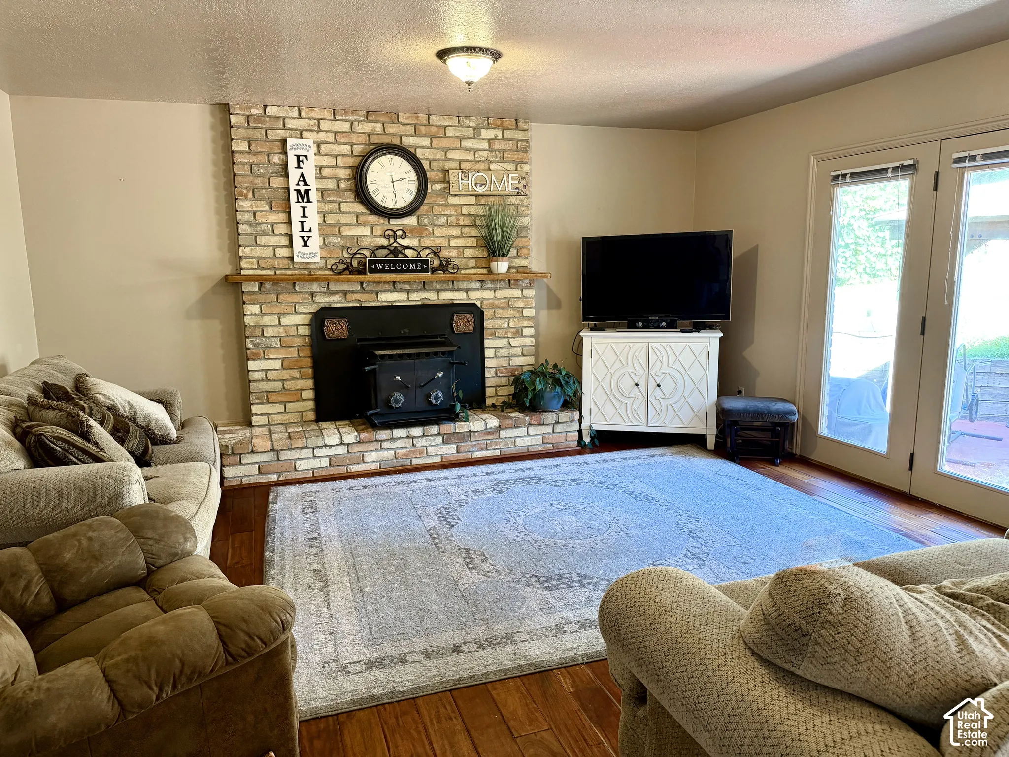 Brick-clad fireplace with a wood-burning insert, hardwood flooring, and double patio doors