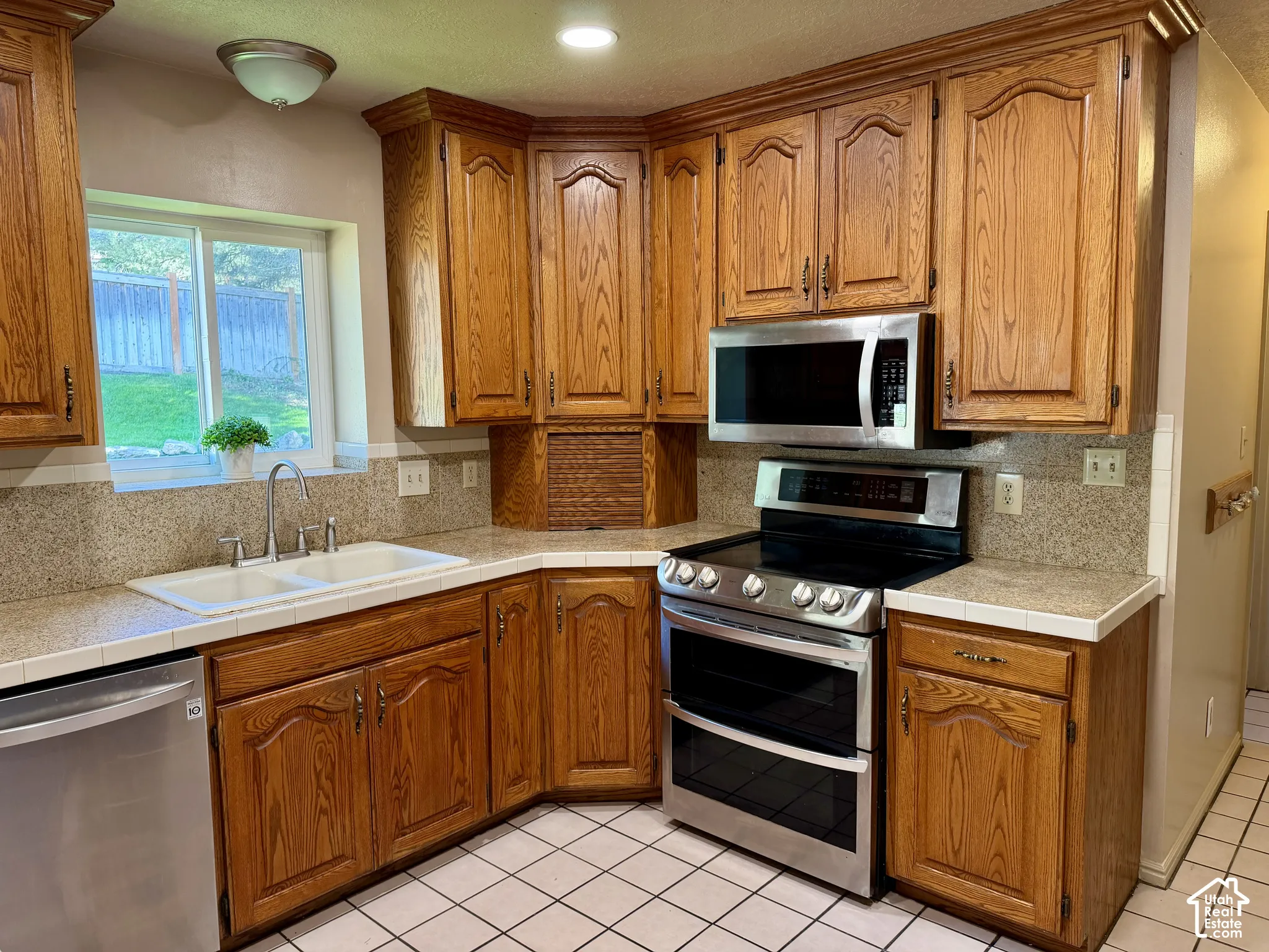 Wood-finish cabinetry, double oven, stainless steel appliances, and white tile flooring