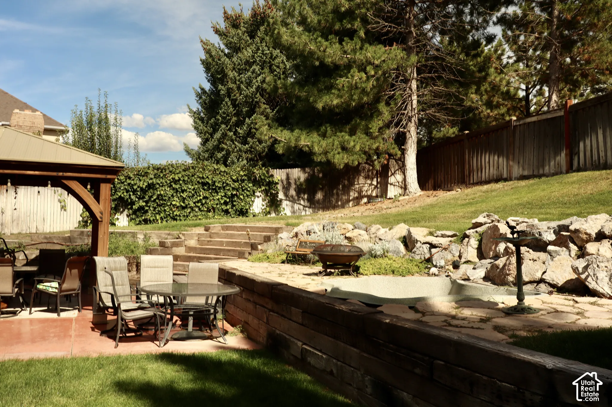Expansive terraced yard with a wooden gazebo, a rock garden, and mature trees