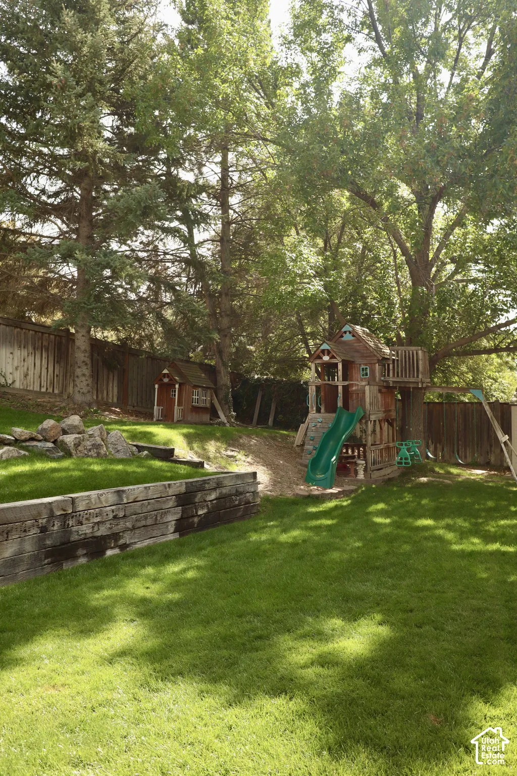 Expansive backyard featuring a manicured lawn, established mature trees and wooden play house with slide.