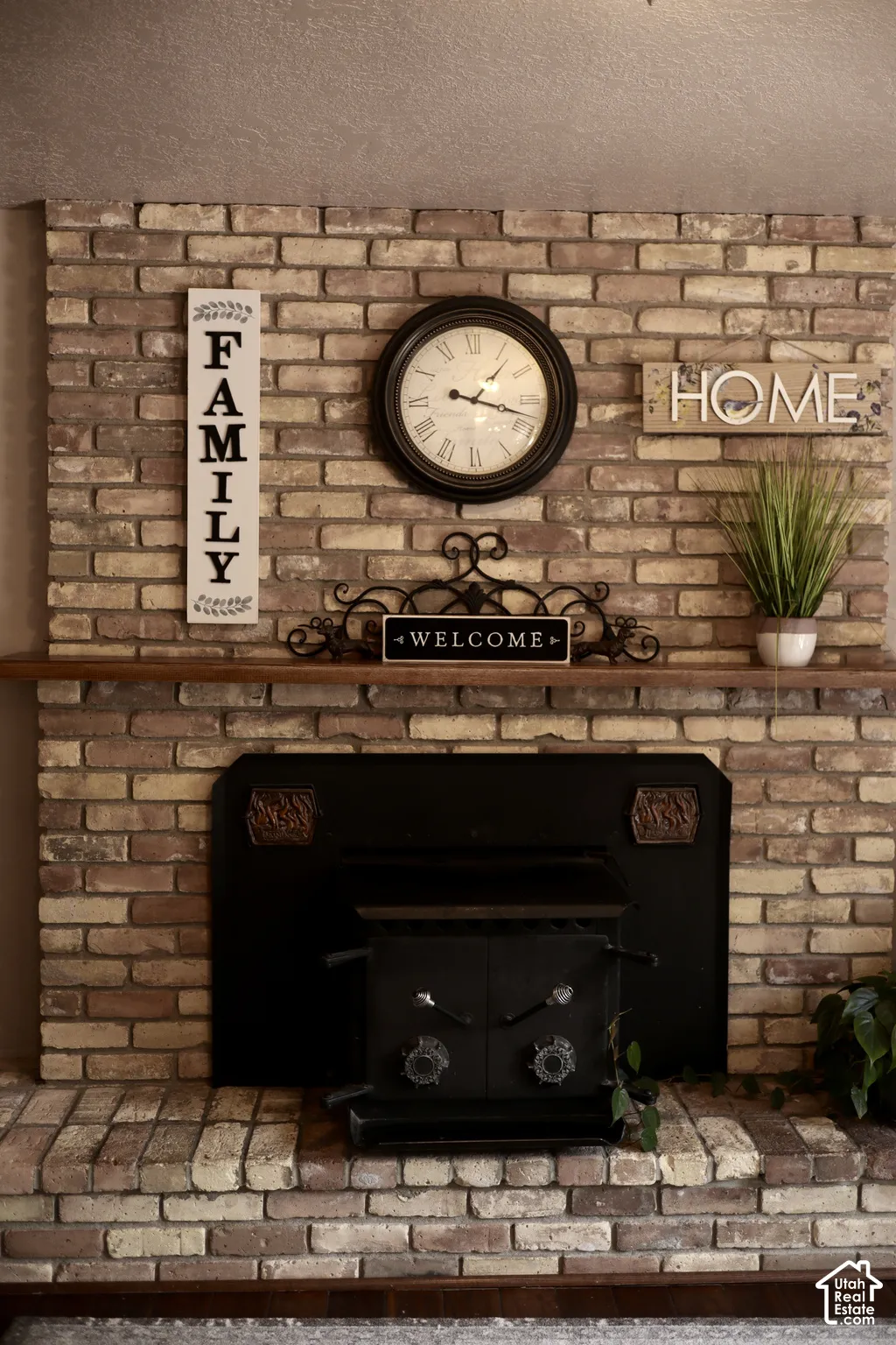 Brick fireplace featuring a hearth, mantel shelf, and a black wood-burning stove insert