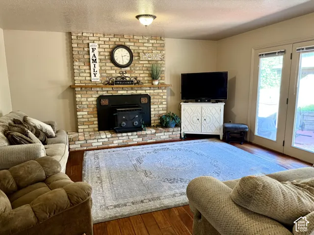Brick-clad fireplace with a wood-burning insert, hardwood flooring, and double patio doors
